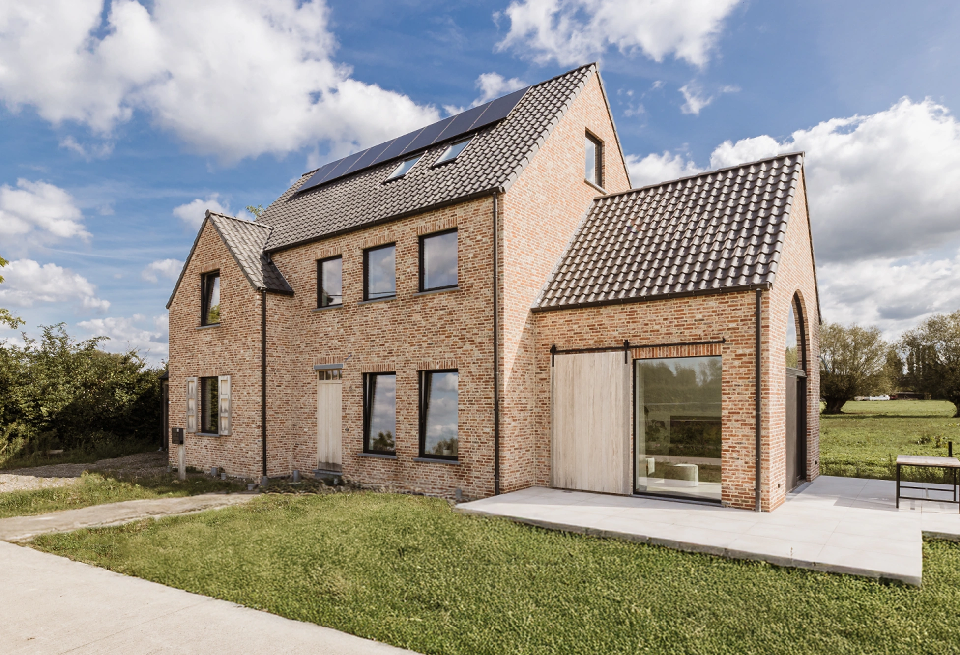 Klassieke bakstenen langgevelwoning met zonnepanelen, terras en grasveld omringd door velden